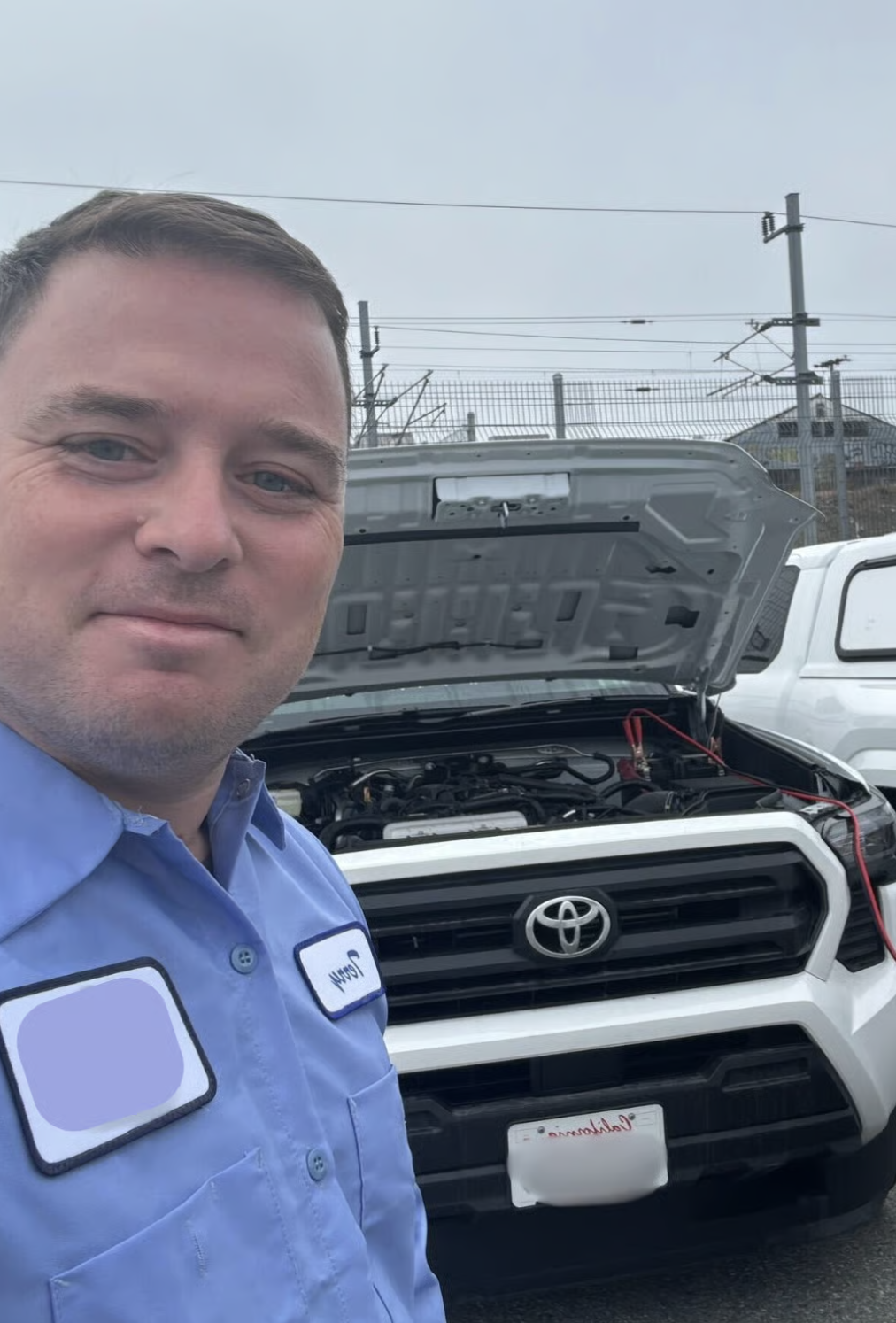 Terry Clarke in uniform next to a company Toyota truck with the hood up and jumper cables attached